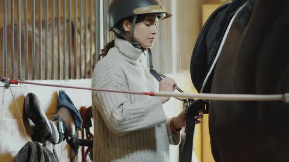 Woman Fastening Straps while Saddling Horse