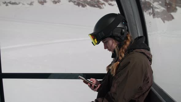 Woman In Skiwear Looking Up From Phone In Cable Car