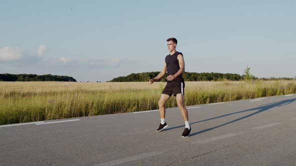 Athletic Man in Sportwear Doing Fast Squats with Jumps on a Path at Nature