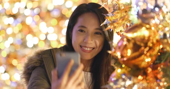 Woman taking selfie on mobile phone with Christmas tree decoration