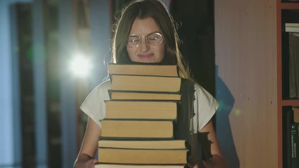 Cheerful Female Student Holds Stack of Books in Her Hands and Laughs in Library