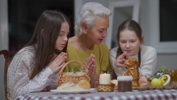 Confident Caucasian Woman and Girls Praying Sitting at Dinner Table Indoors on Easter Sunday