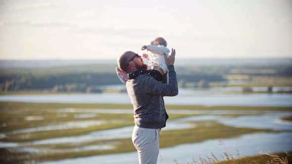 Young Father Playing with His Baby Daughter on the Wheat Field - Holding Her on His Hands