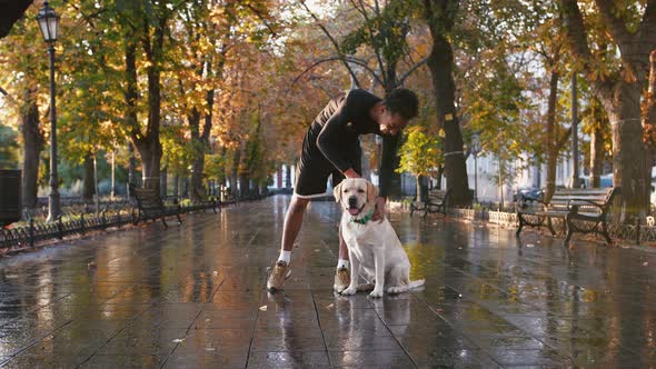 Portrait of Young Black Man and His White Labrador Dog in City Park During Beautiful Autumn Morning