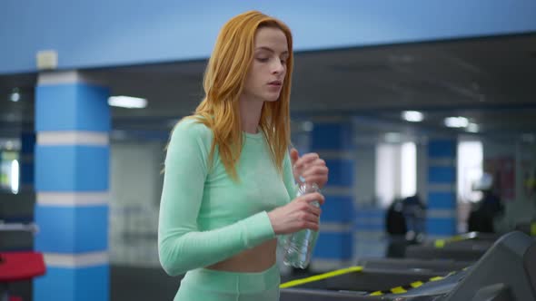 Slim Fit Redhead Young Caucasian Woman Walking with Water Bottle Start Running on Treadmill in Gym