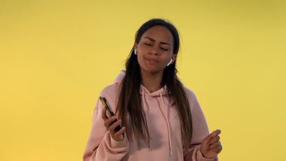 Cheerful African Girl Listening To the Music in Wireless Headphones on Yellow Background