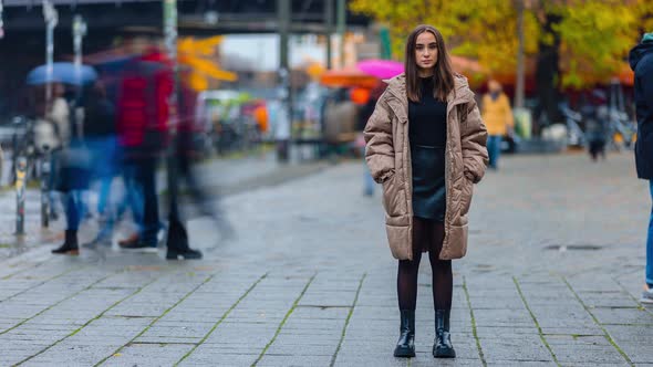 Time lapse of young woman standing in city street on autumn day looking at camera alone