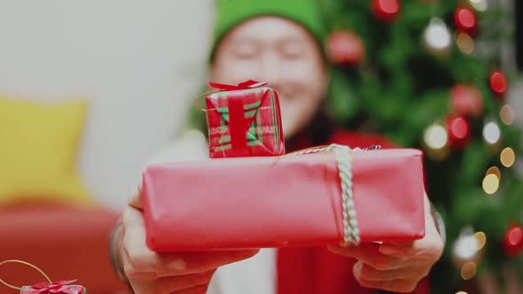 Asian man presents a red gift box in front of the camera.