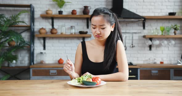 Asian Woman Sitting at Table Looking Sad and Bored with Diet Not Wanting to Eat Salad