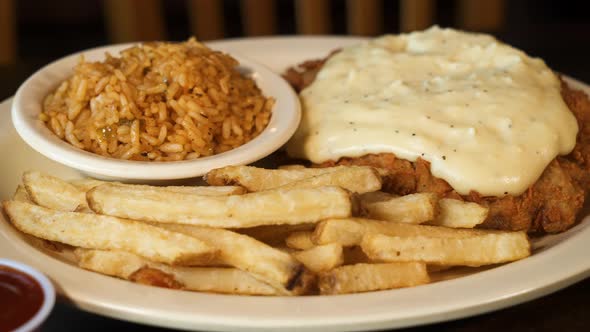 Chicken fried steak smothered in peppered country gravy with dirty rice and french fries, slider clo