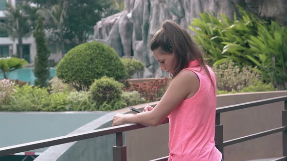 Slim Girl with Smartphone Holds on Handrail in Exotic Hotel