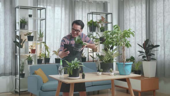 Asian Man Waving Hands And Talking While Live Stream Selling Plants By Smartphone At Home