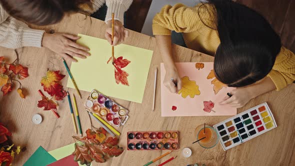 Unknown Mom and Kid Girl Drawing Autumn Leaves While Sitting at Wooden Table