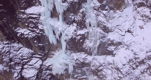 Aerial drone view of a man ice climbing on a frozen waterfall in the mountains