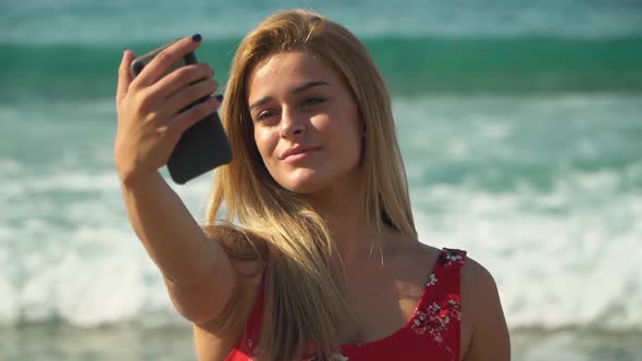 Young Beautiful Girl Posing Makes Selfie on the Background of a Beautiful Sea with Waves