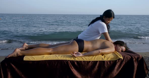 Close-up Massage on the Beach on a Special Table. Asian Masseuse Massages the Whole Legs and Back of