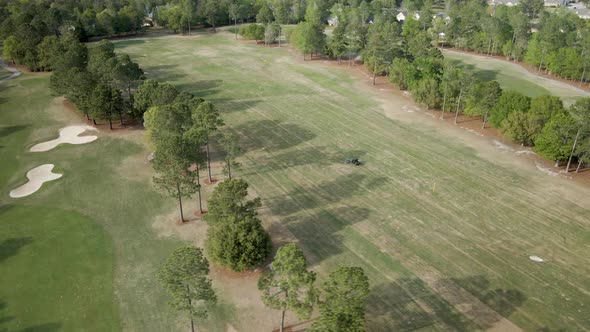 Golf cart driving alongside gold course Wide aerial shot