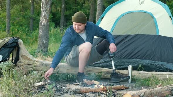 Disabled man with prosthetic leg is sitting on wooden log in forest near fire.