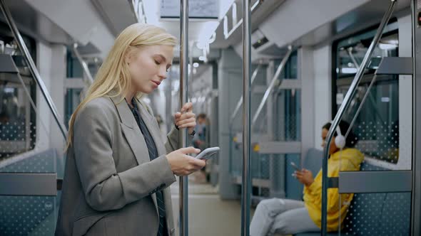 Young Blonde Girl Standing in Modern Metro Looking at Her Phone and Texting