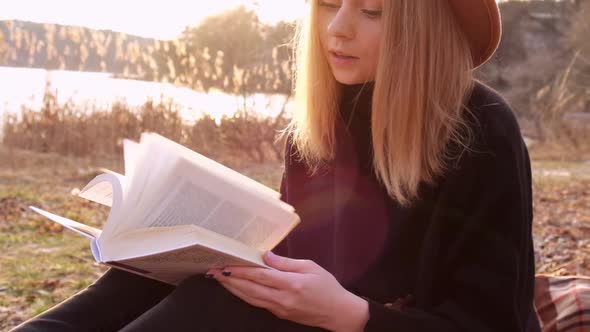 Slow Motion Caucasian Blonde Woman with Beige Hat in Black Sweater Reads Book in the Countryside