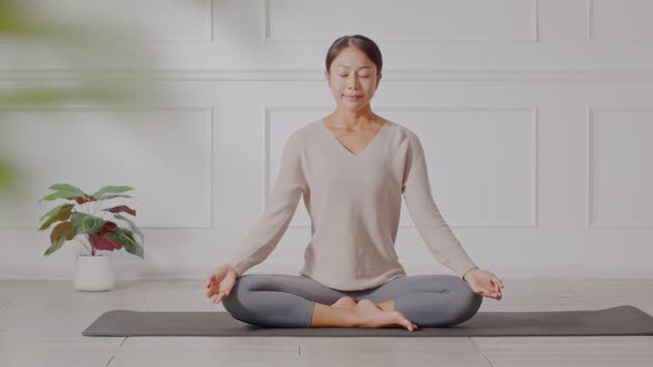 Calm of wellness Asian young woman sit on carpet breathing with yoga lotus pose