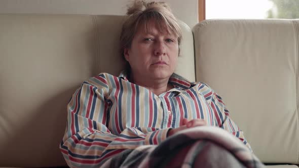 Emotional senior caucasian woman sits on the white sofa at home in front of the TV