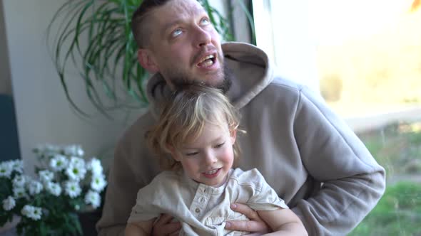 Happy Cheerful Caucasian Man Hugging His Small Cute Son and Laughing at Home