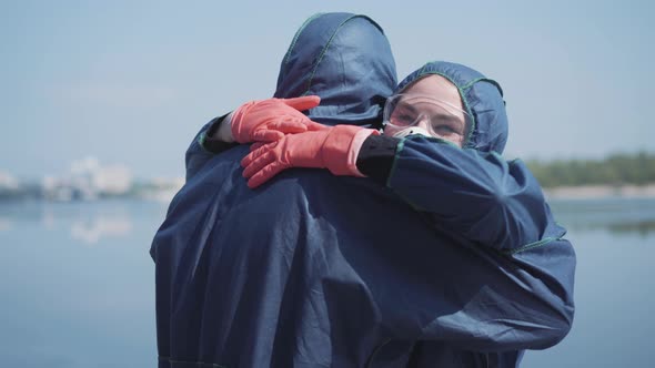 Close-up of Joyful Caucasian Man and Woman in Chemical Suits Hugging Outdoors on Sunny Spring Summer