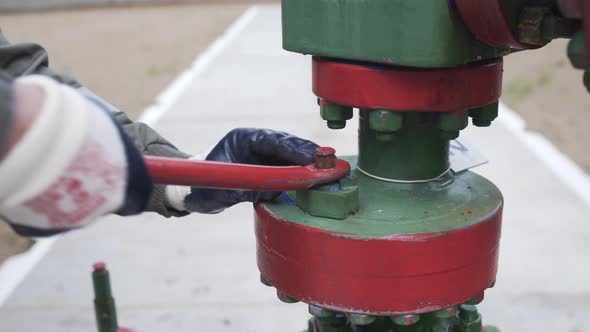 Close Up Shot of Male Hands in Protective Rubber Gloves Closing Valve of Wellhead To Shut Off Well