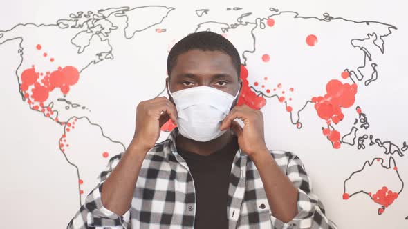 African American Male in Medical Mask Looks at Camera Against Background of Map of Spread of