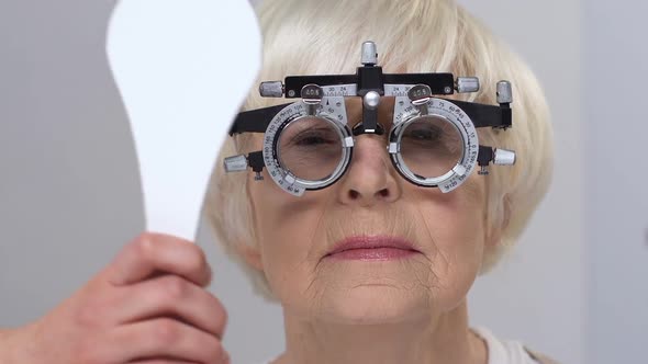 Smiling Elderly Woman Wearing Phoropter Closing One Eye, Vision Examination