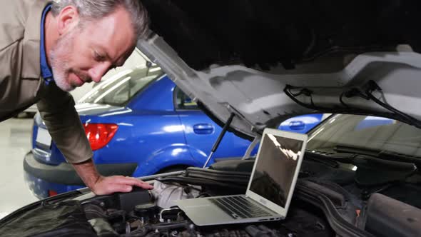 Mechanic using laptop while servicing a car engine