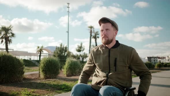 Confident Bearded Man Is Riding on Wheelchair Outdoors Alone in Sunny Day