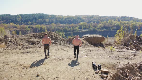 Active sportsmen without shirt show their trained body standing at the edge of a hill.