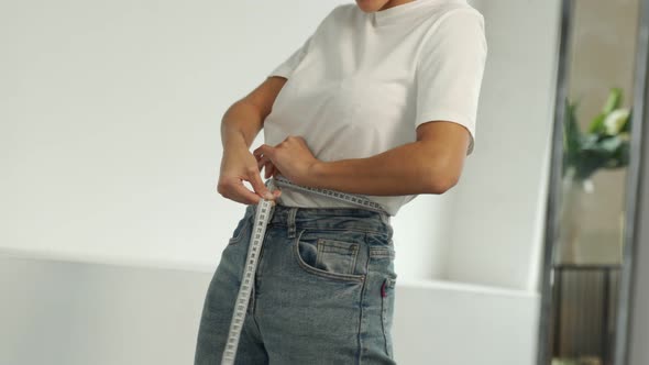 Slender Black Woman Standing in Front of a Mirror Measures Her Waist with a Measuring Tape After