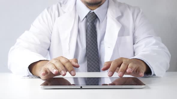 The doctor sat at the table typing data on the tablet for the treatment of patients.