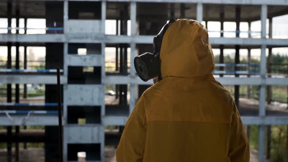 Human in Gas Mask and Yellow Protective Suit Sits in Abandoned Building Looks Into Distance and