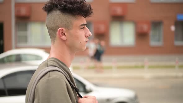 A young man with a backpack looks in front of him, a side view