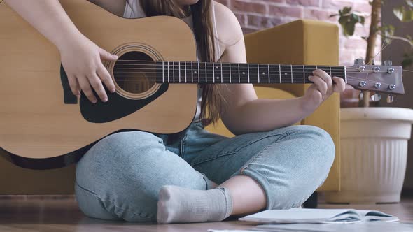 Woman Plays Guitar and Writes Down Important Things in Notebook Sitting in Lotus Position Closeup