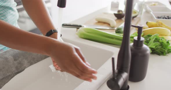 Midsection of african american woman washing hands in sink in kitchen