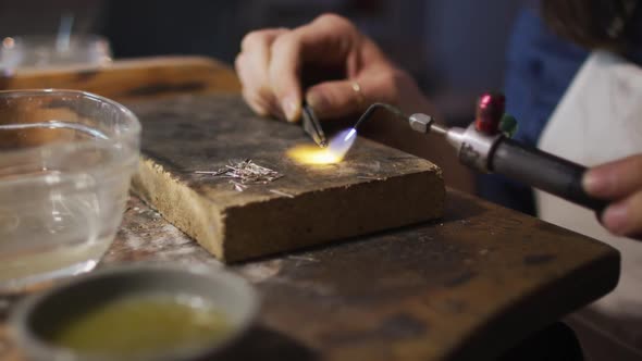 Close up of hands of caucasian female jeweller using gas burner, making jewelry