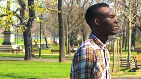 A Young Black Man Walks Back and Forth in a Park on a Sunny Day and Broods Over Something