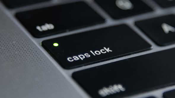 Finger presses the Caps Lock Button on laptop keyboard.