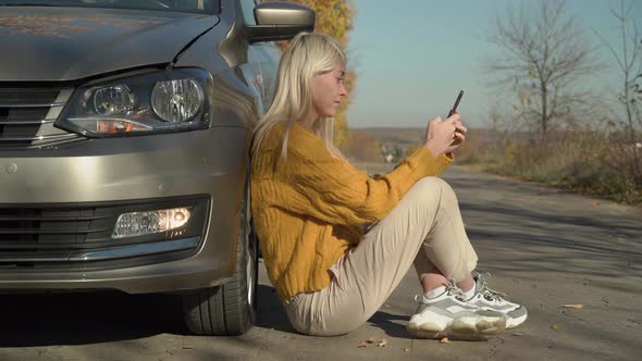 A young woman calls the emergency services near a broken car.