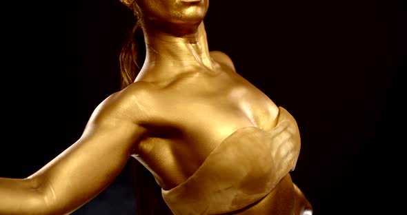 Golden Painted Woman Is Dancing in Studio in Black Background, Skin Is Glowing By Pigment