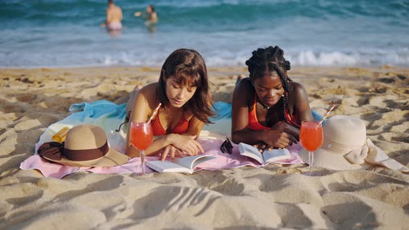 Two Student Girls Lying on Sandy Beach with Open Books
