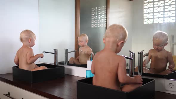 Two Caucasian Twin Toddlers Sitting in Sinks Playing with Water and Brushing Their Teeth