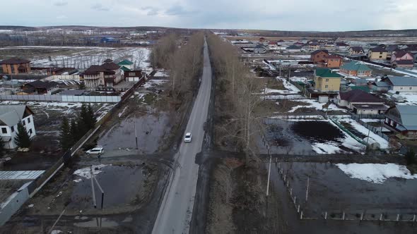 Aerial view of a white car drives along a road and enters a cottage village 03