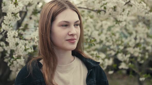 Beautiful young woman in a dark denim jacket in the spring garden in bloom