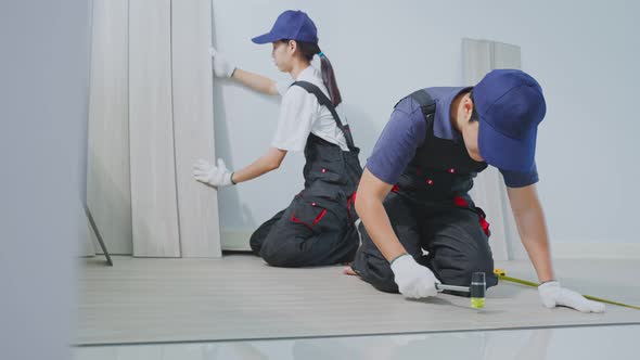 Asian Craftsman worker people work to repair corridor installs laminate board on floor at home.